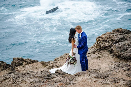 a man and woman in a suit and suit standing on a cliff overlooking water