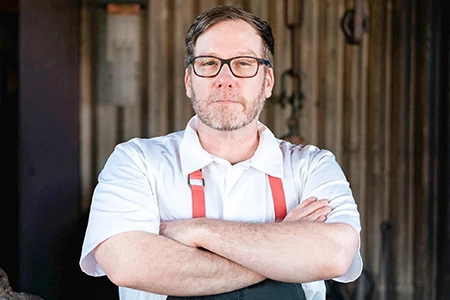 a man with glasses and a beard wearing a white shirt and red suspenders