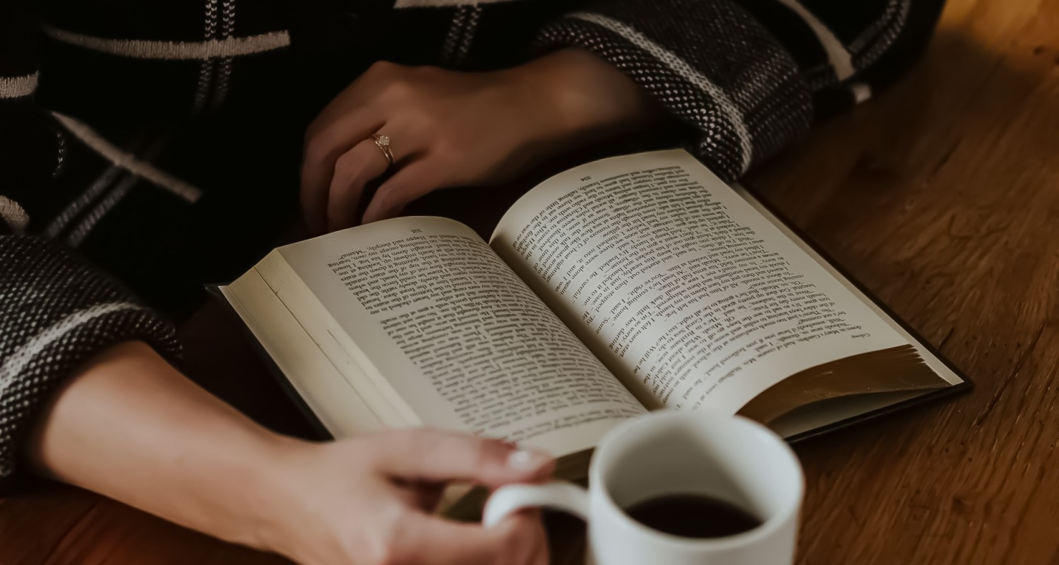 a person holding a book and a cup of coffee