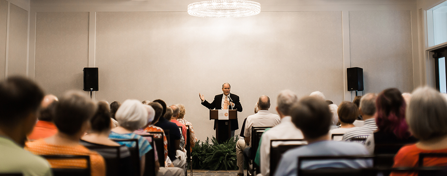 a man standing at a podium with a microphone and a crowd of people