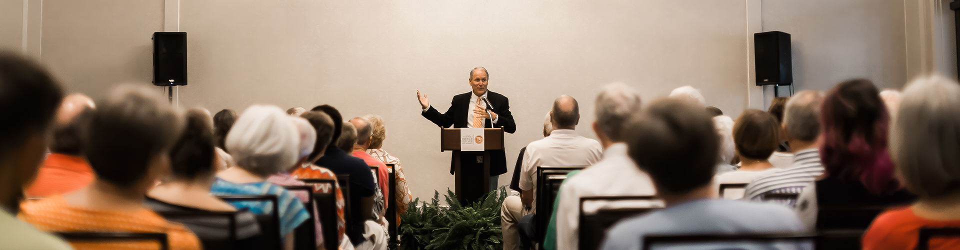 a man standing at a podium with a crowd of people in the background