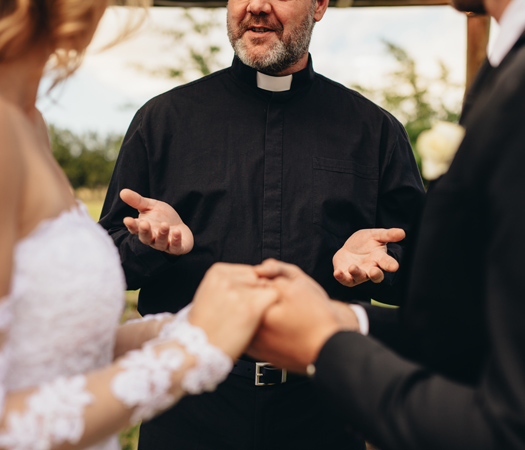 a man in a black robe holding hands with a bride and groom in the background