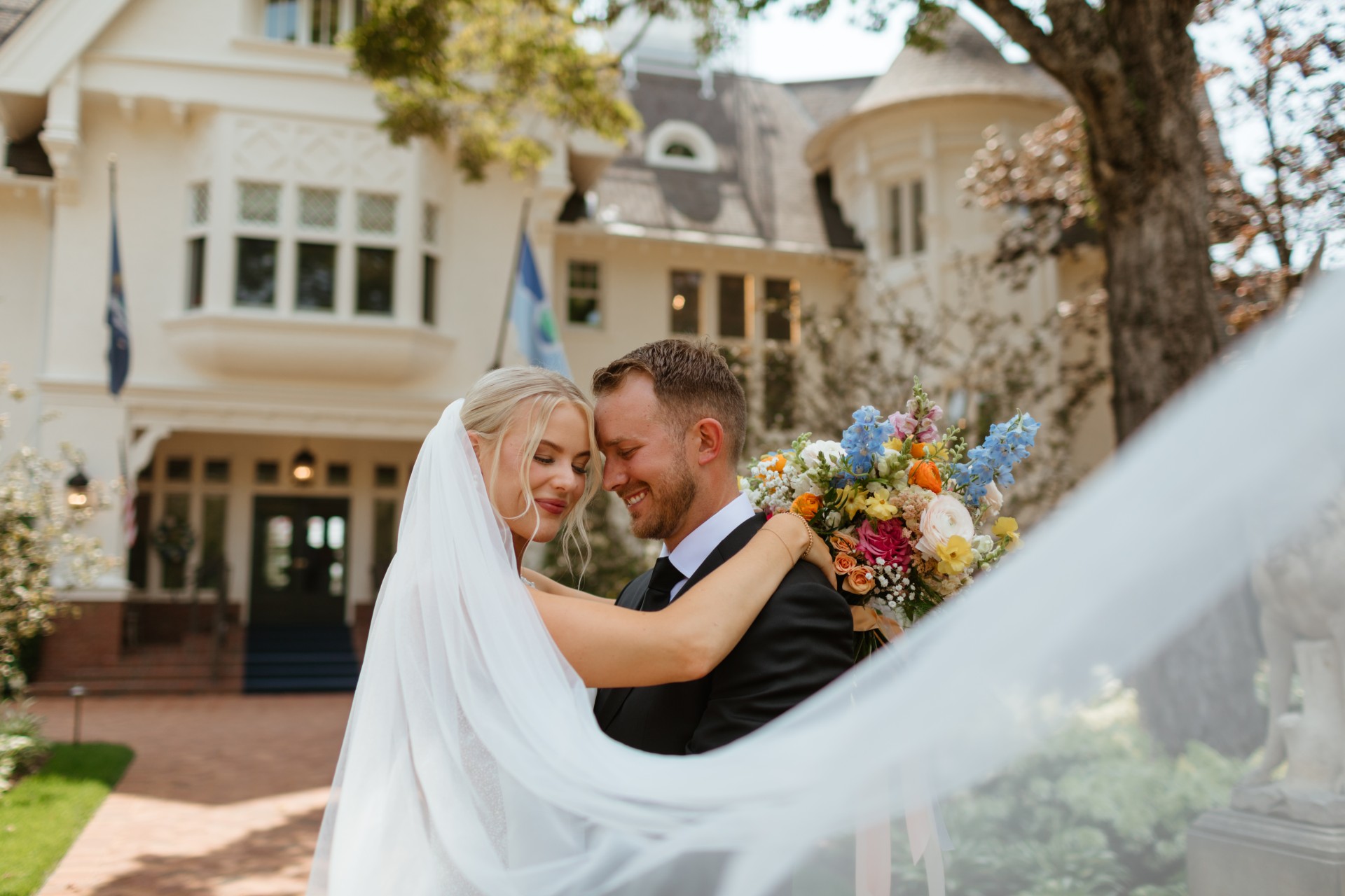 Bride and groom embracing outside The Inn at Stonecliffe’s historic mansion on Mackinac Island, with a colourful bouquet and the resort’s elegant façade in the background, showing the romantic atmosphere of a luxury boutique wedding venue.