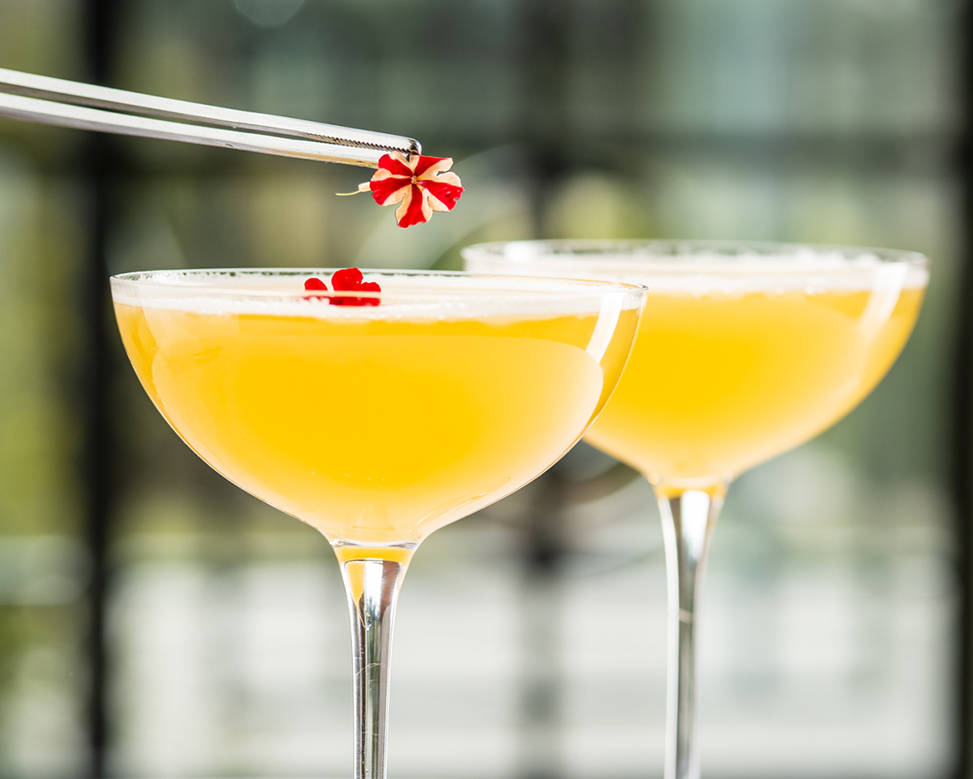 a pair of glasses with yellow liquid and a red flower on top