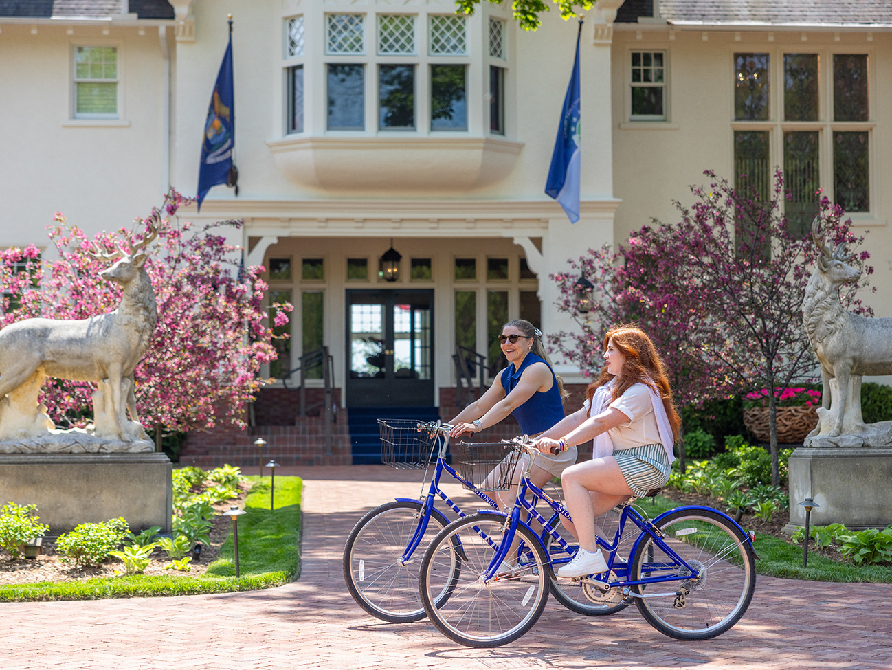 two women riding bicycles in front of a house