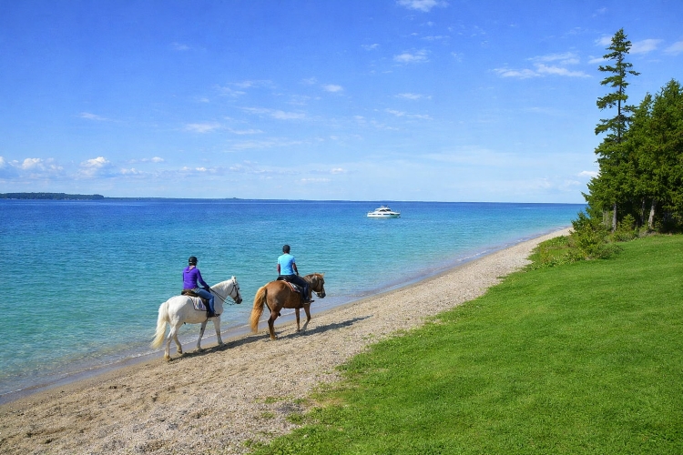 Two horseback riders following the Lake Huron shoreline toward British Landing on Mackinac Island, near The Inn at Stonecliffe.