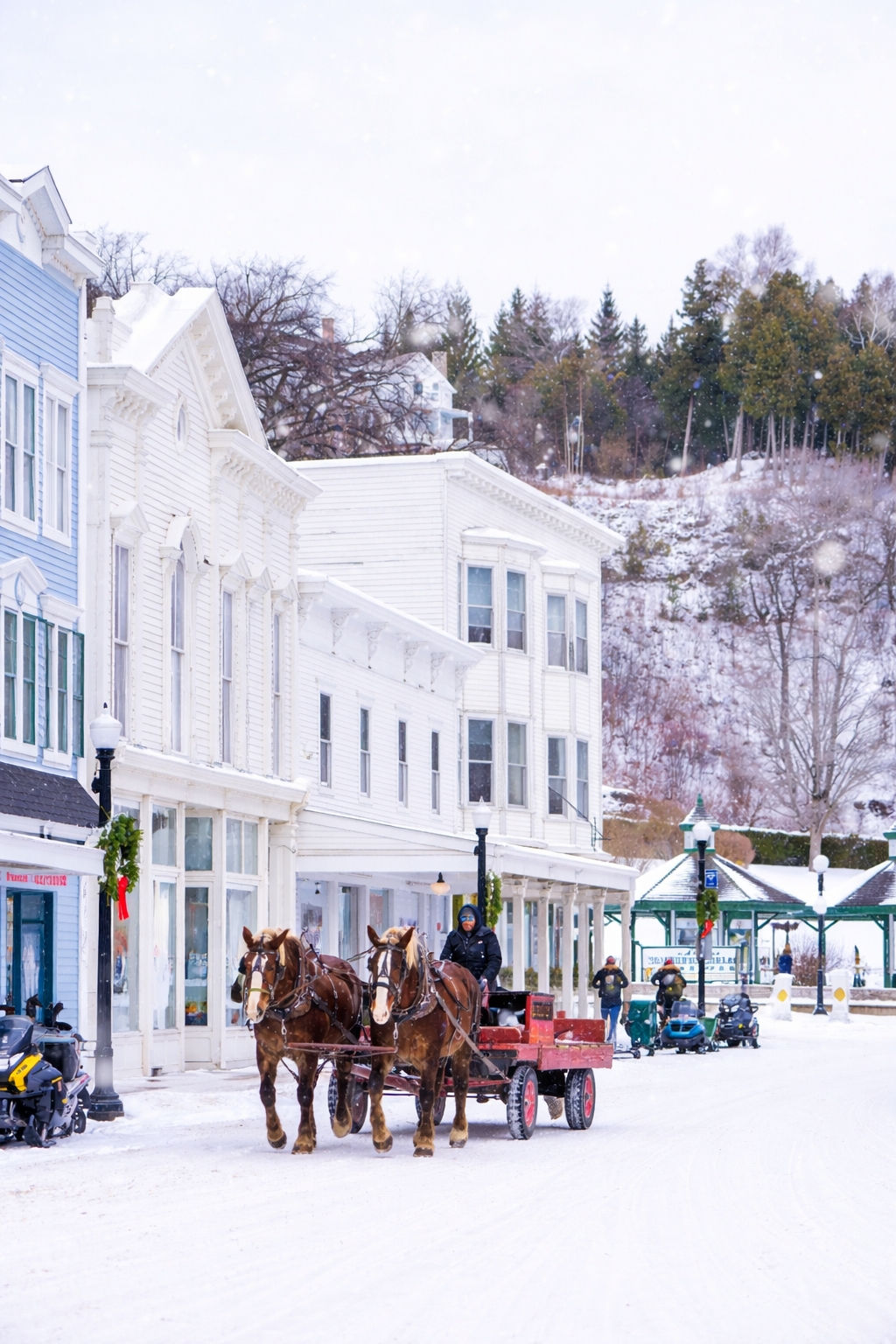A winter view of Mackinac Island showing snow-covered Main Street, parked snowmobiles, and a quiet horse-drawn sled scene with no crowds.