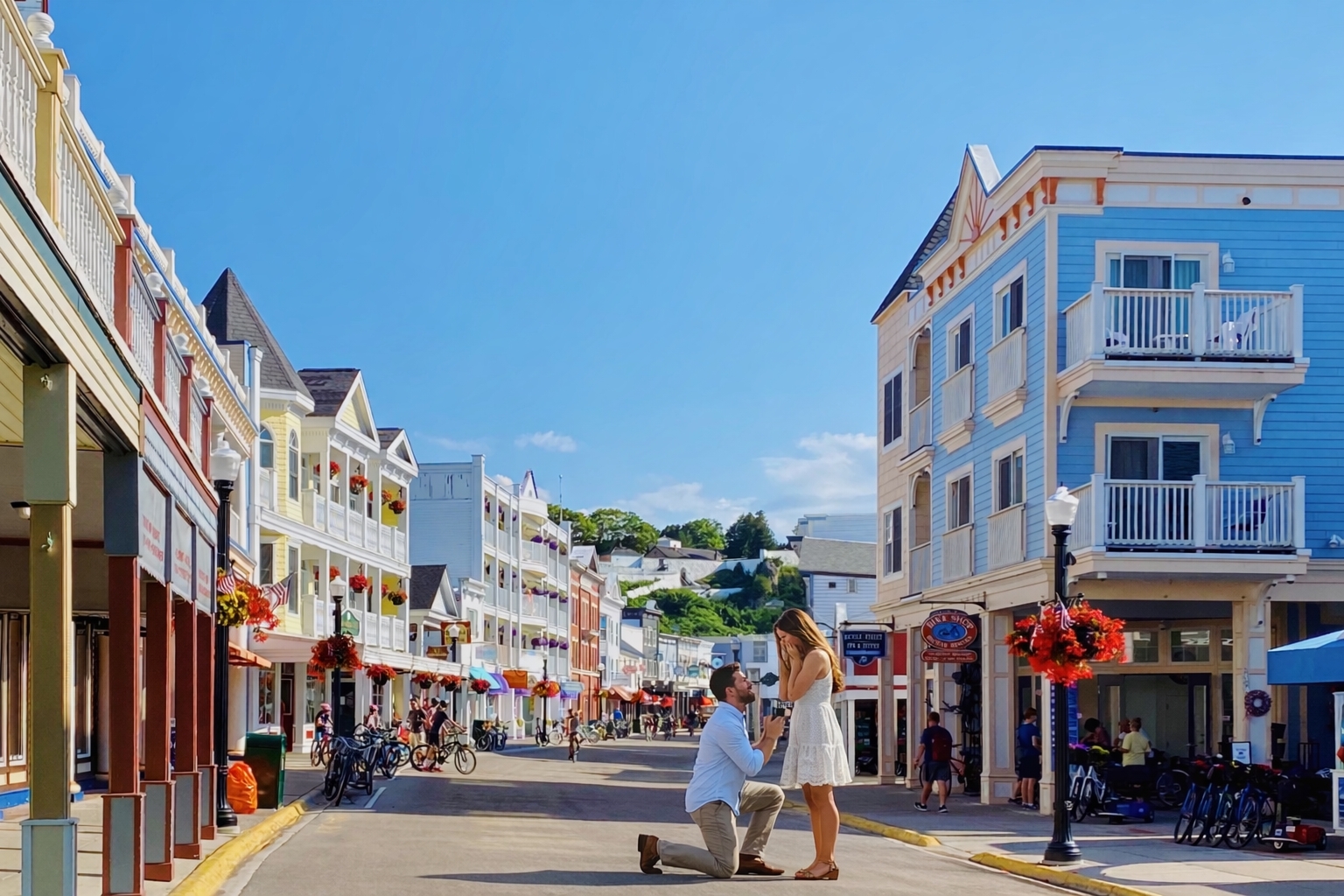 Colorful downtown Mackinac Island street scene with historic Victorian buildings, bicycles, and a man kneeling to propose to his fiancée in the middle of the car-free Main Street district, capturing a romantic engagement moment at one of the most iconic p