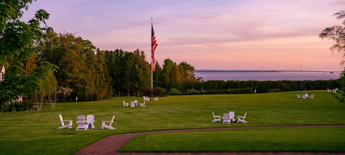 a lawn overlooking great lake with white chairs at sunset