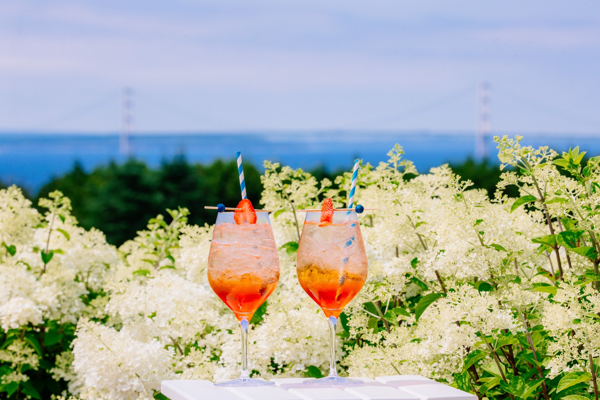 two glasses of drinks with straws on a table with white flowers