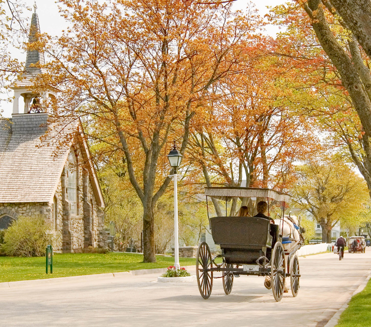 Horse-drawn carriage ride on Mackinac Island in autumn, passing historic stone buildings and colorful fall foliage near The Inn at Stonecliffe.