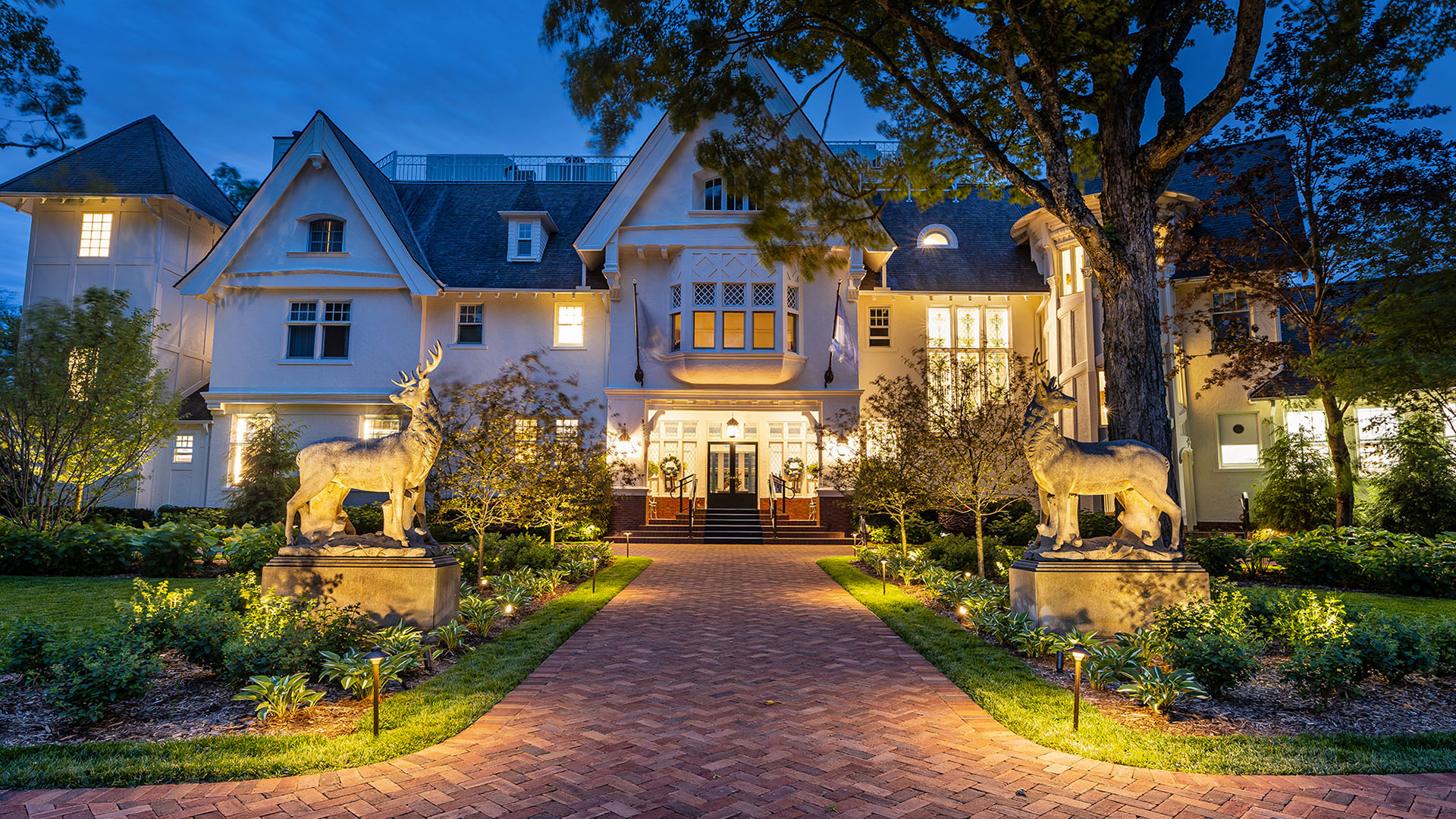 The Inn at Stonecliffe Mansion on Mackinac Island illuminated at dusk with grand statues and landscaped entrance.