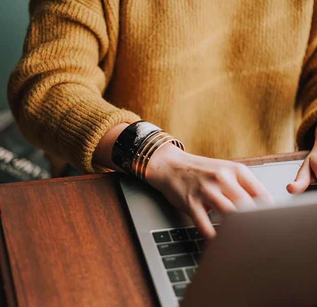 close up of a lady typing on her laptop at a wooden table