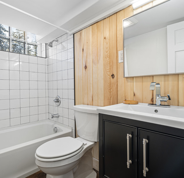 2 bedroom apartment, white tiles. a vanity with a mirror and a sink and toilet and a small window with pretty sunlight shining through