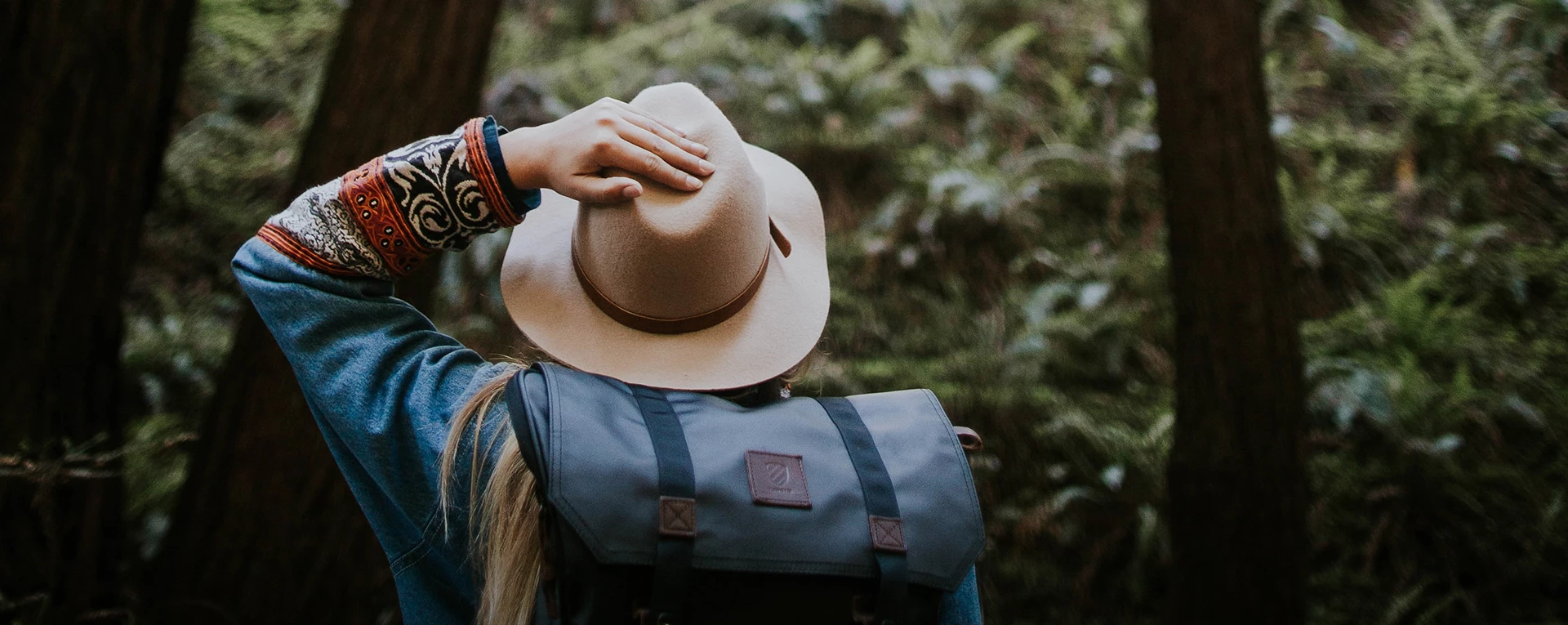 lady grabbing onto her hat as she hikes through the forest