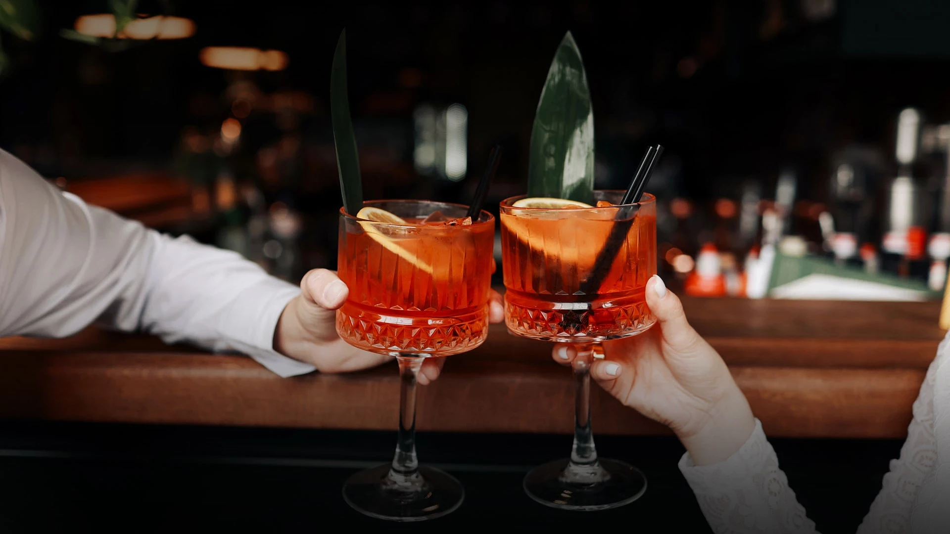 two hands holding glasses with orange liquid and a leaf