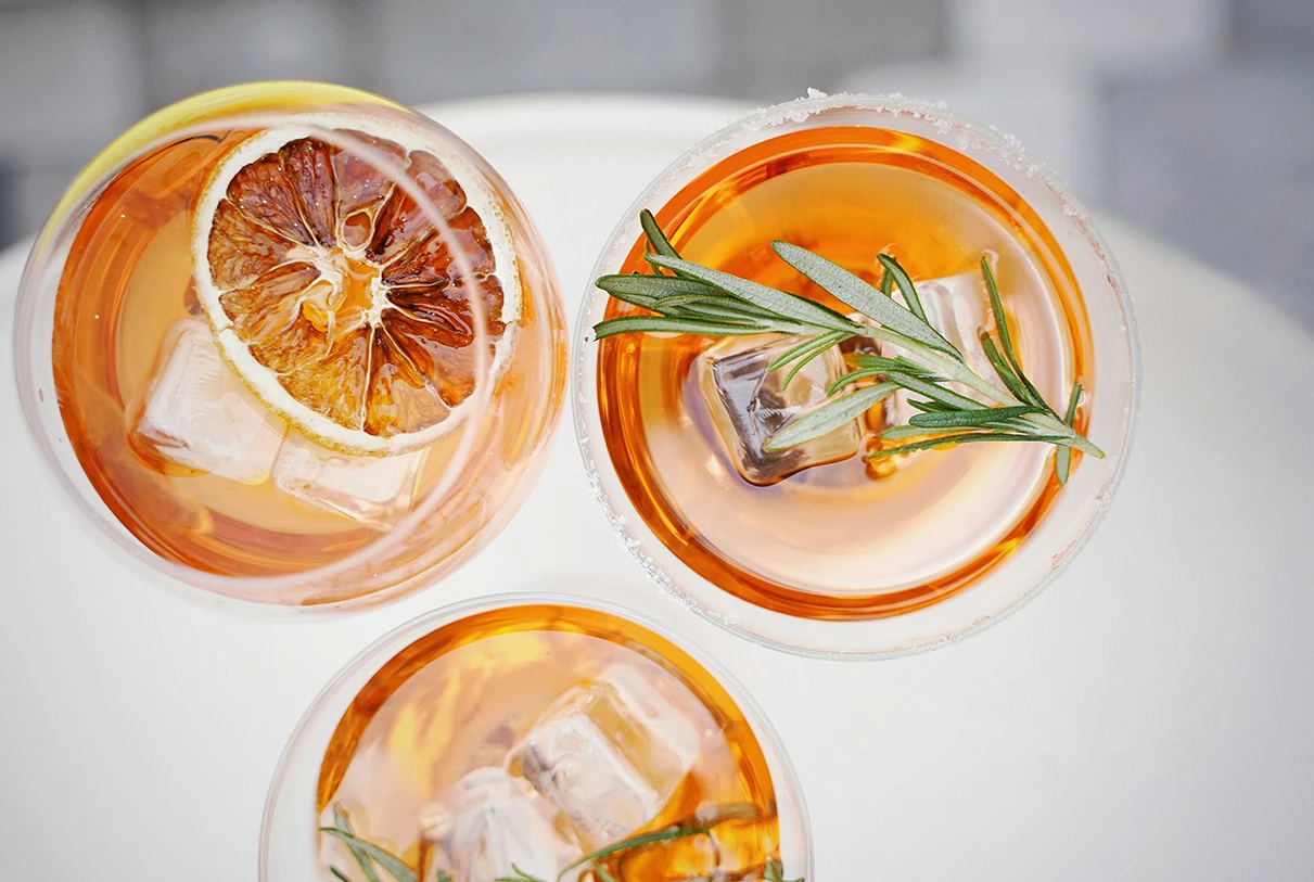 a group of glasses with drinks and a rosemary branch