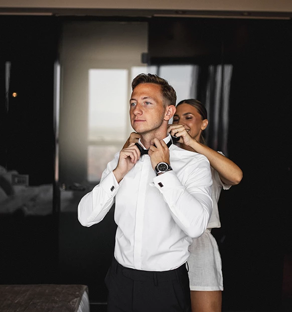 a woman helping a man to tie a bow tie