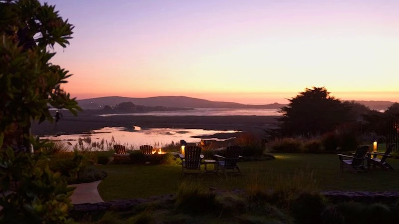 view of the ocean and mountains during the sunset with chairs and bonfire