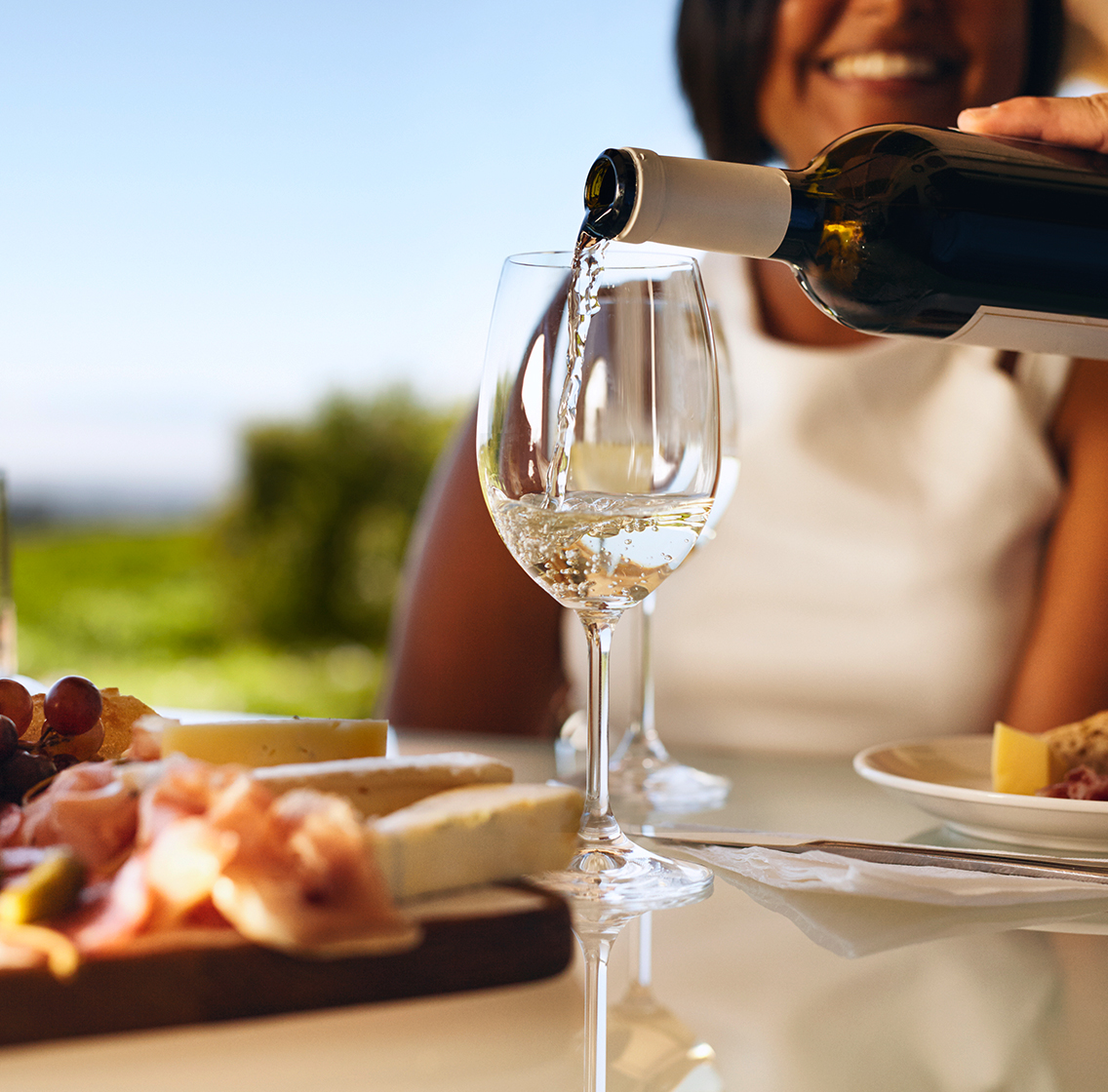 white wine being poured into glass next to a cheese board