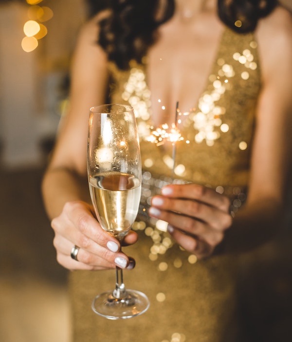 woman wearing gold dress holding champagne and a sparkler for new years
