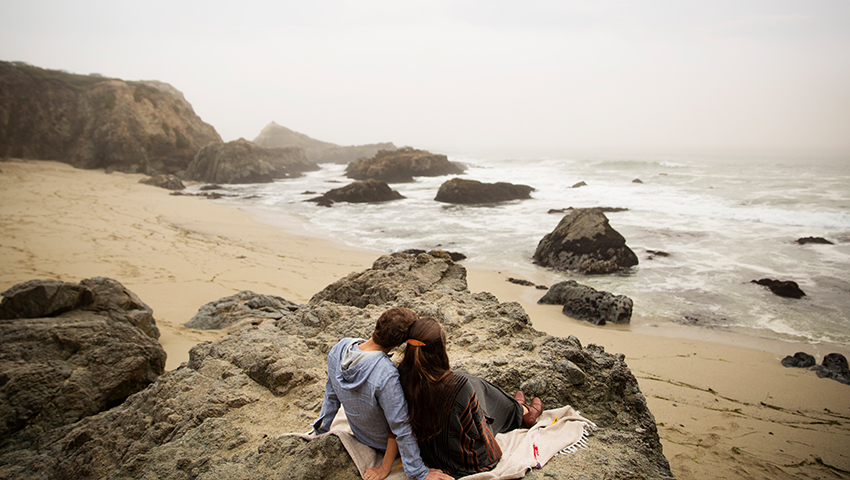 man and women sitting on cliffs by the beach