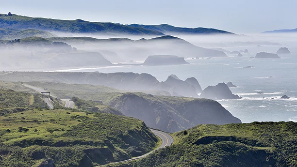 a road going through a valley with water and fog