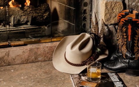 a hat and a glass of liquid next to a fireplace