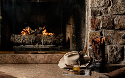 a cowboy boots and a hat by a fireplace