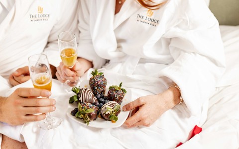 a couple of people in bed with a plate of chocolate covered strawberries and champagne