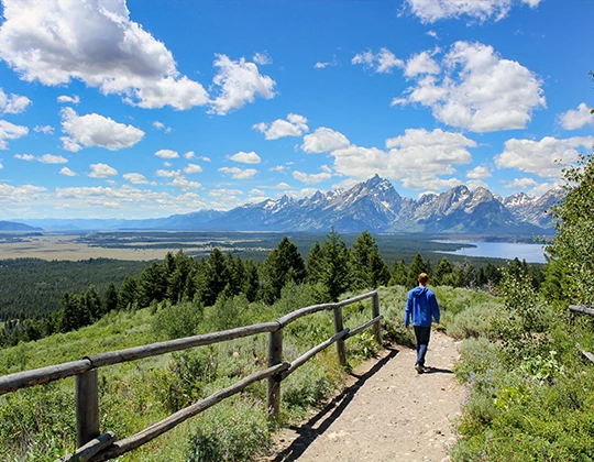 a person walking on a path with a fence and mountains in the background