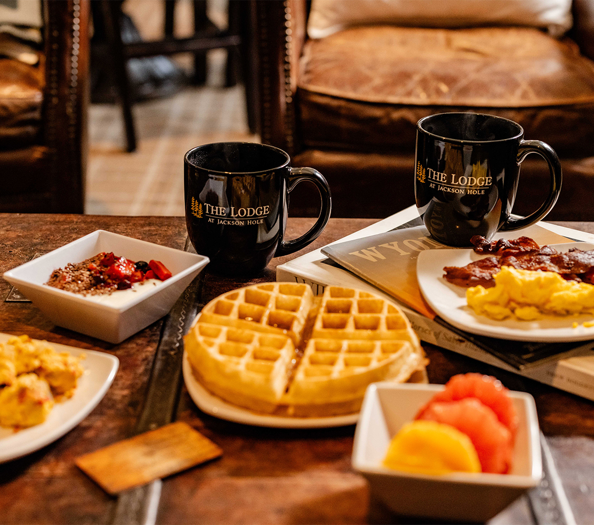 a table with plates of food and coffee mugs
