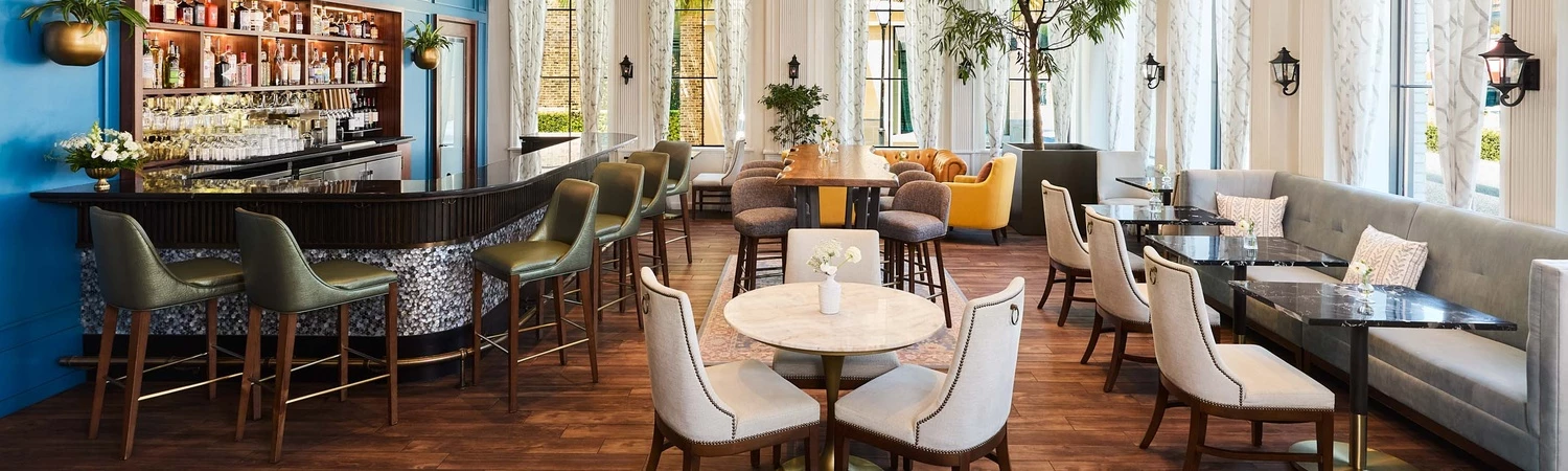 A brightly lit lounge area with a bar, tables, and chairs.