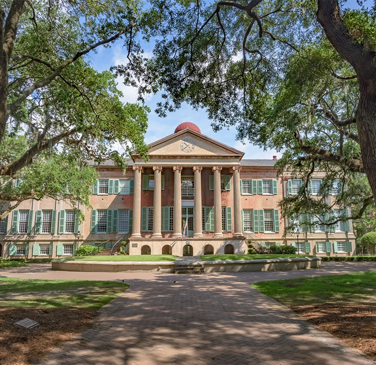 A large building with columns and a clock tower surrounded by trees and a pathway.