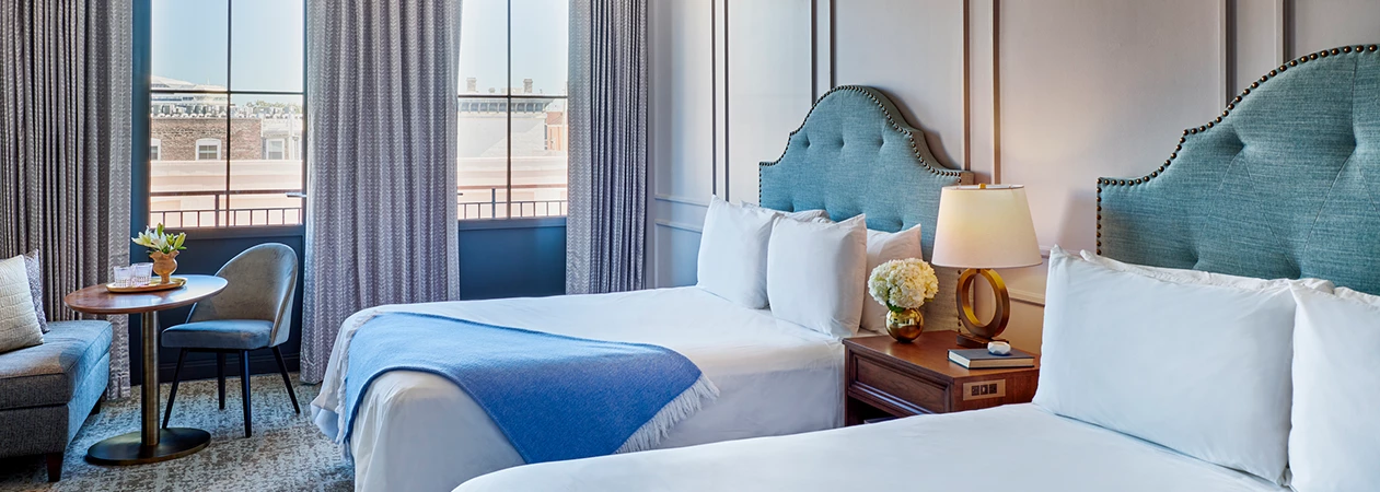 A hotel room with two beds, a small table, and a window