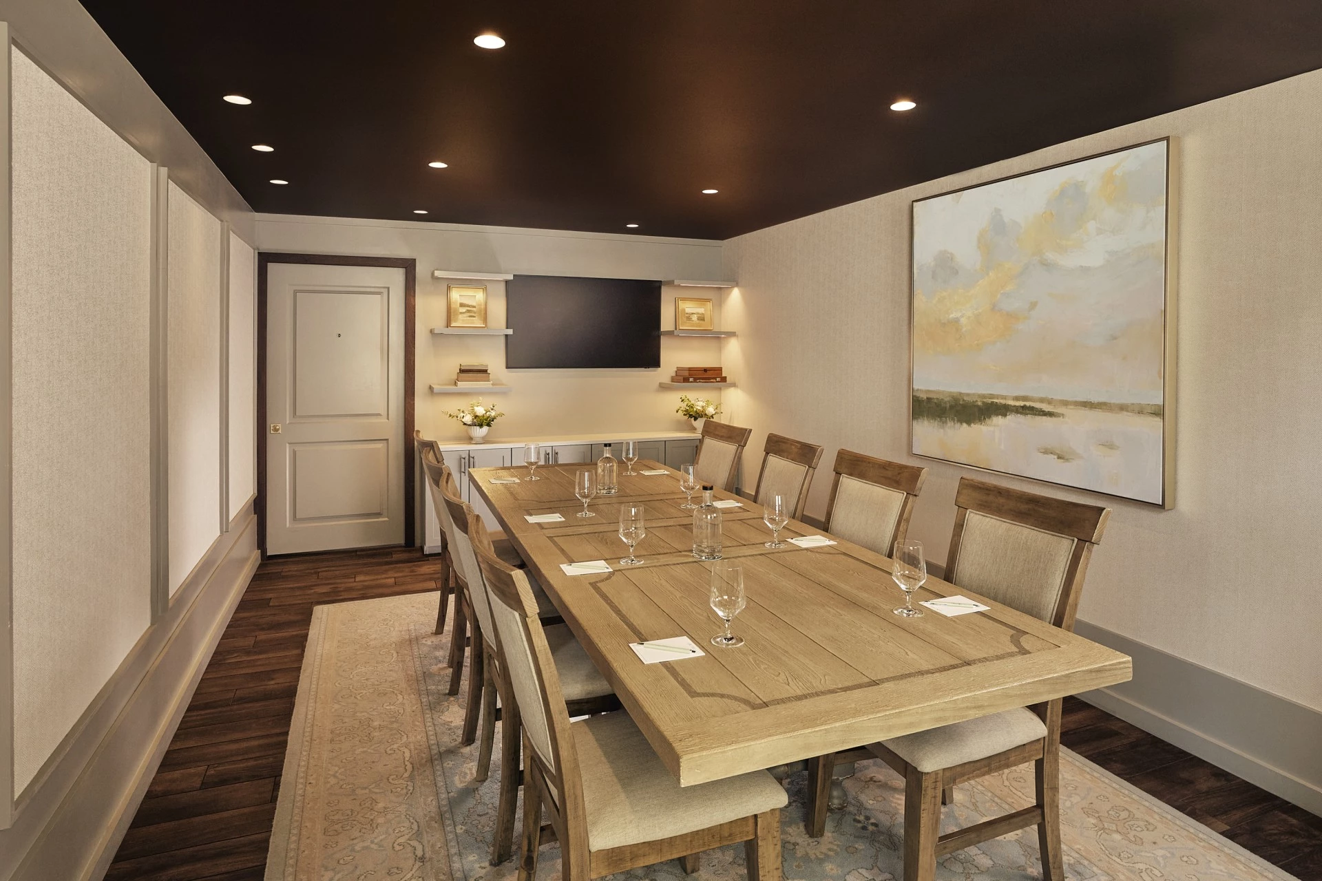 A long wooden table with ten chairs set for a meeting or dining event, with wine glasses and note cards on it.