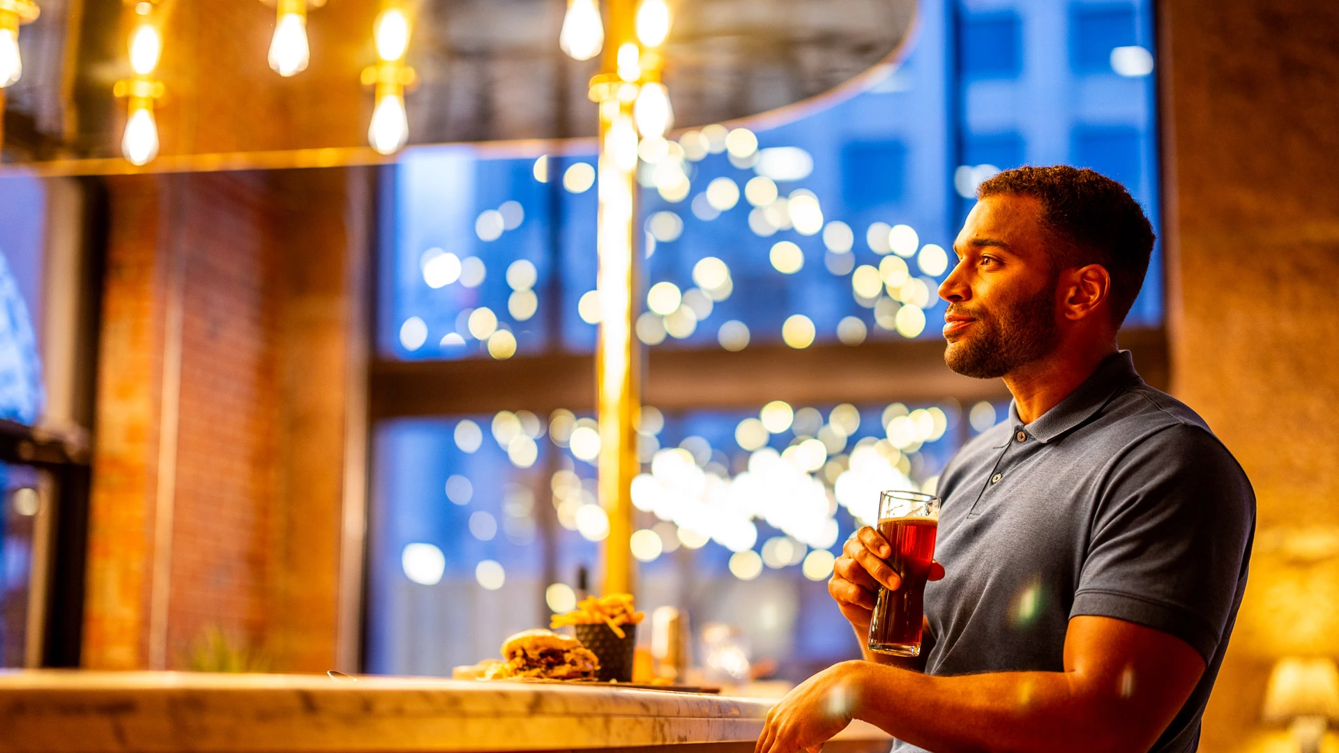 A man sits at a bar with a beer and food