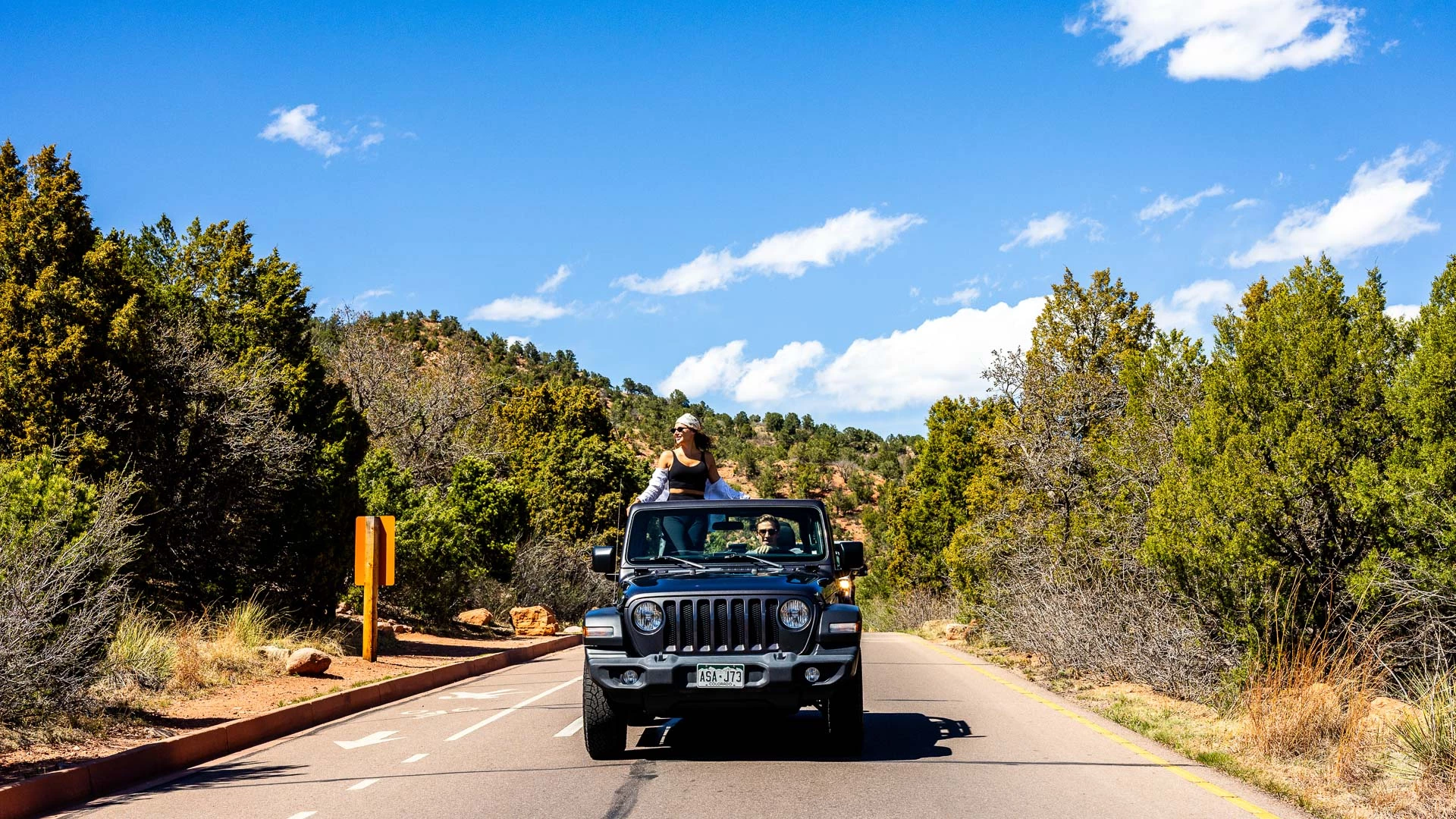 a jeep with people on top is driving down a road surrounded by trees
