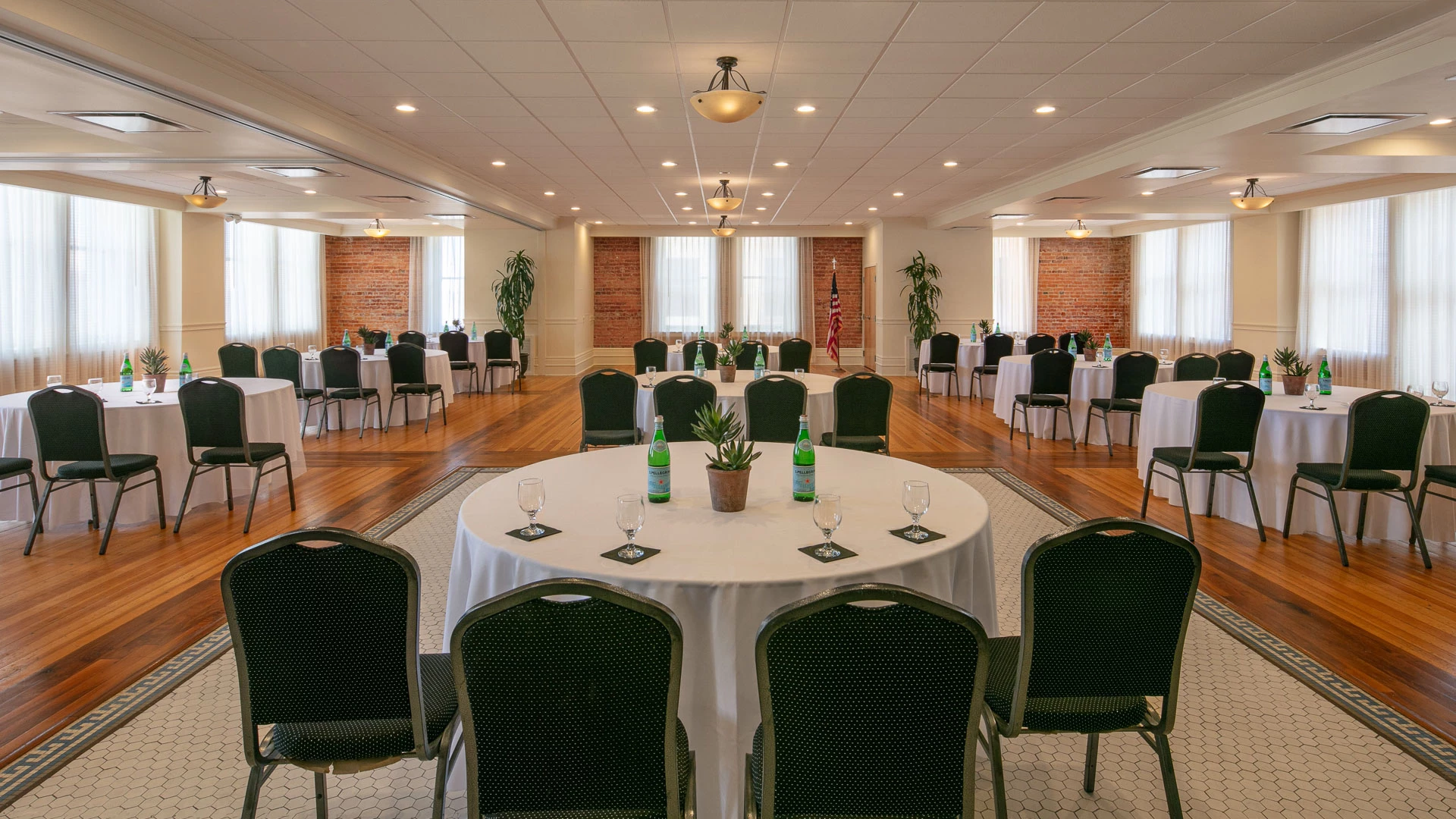 A large meeting room with round tables, white tablecloths, and green chairs.