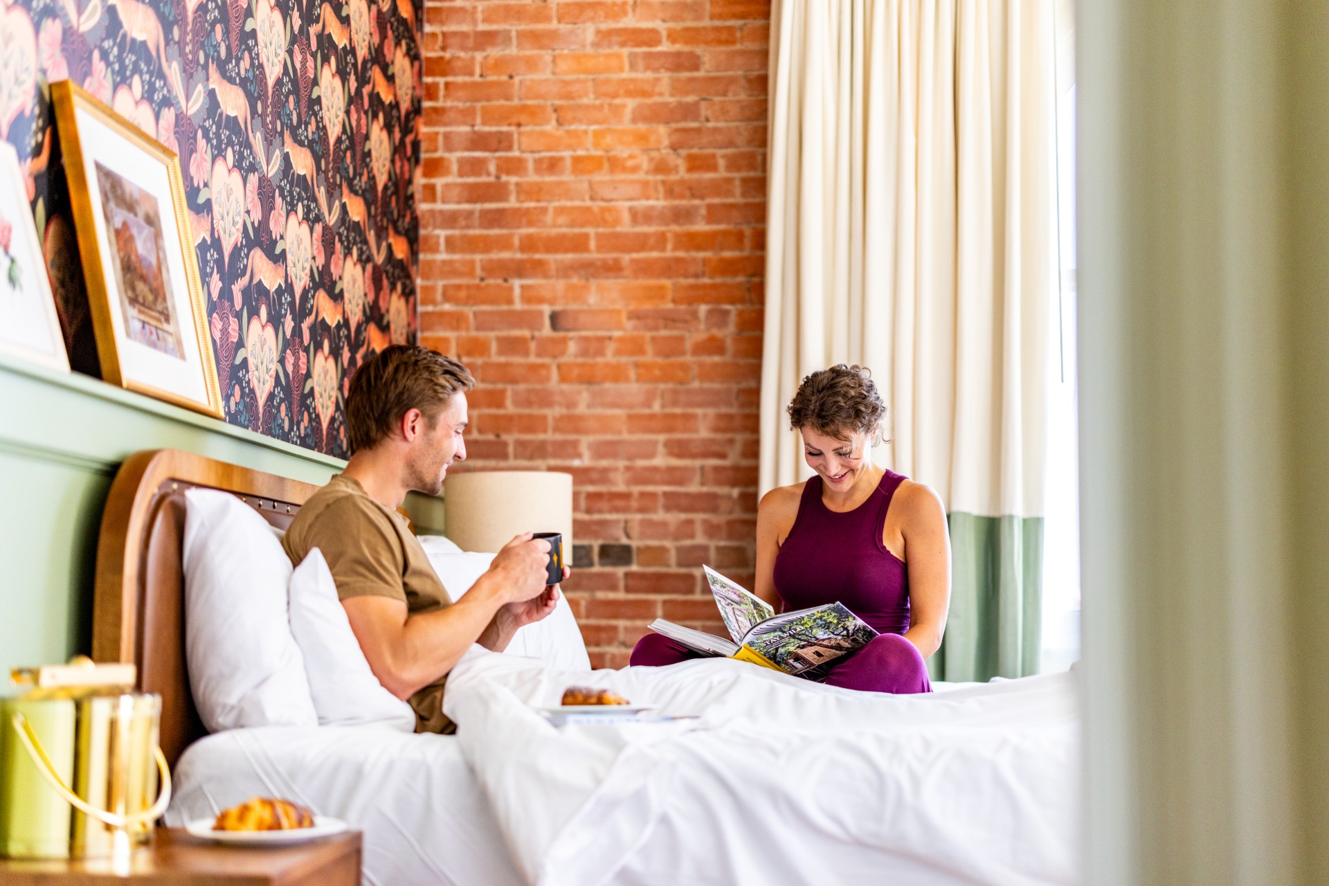 a man and woman sitting on a bed looking at a book