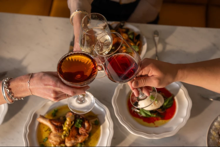 A table with four hands holding wine glasses and plates of food.