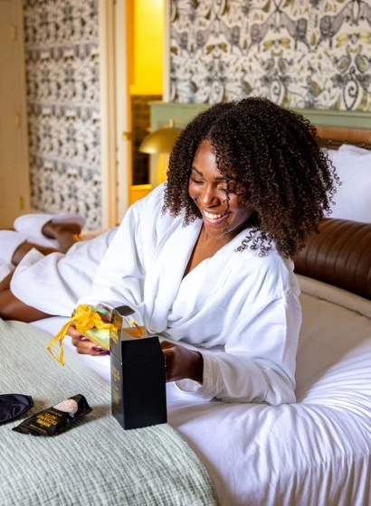 A woman in a white robe sitting on a bed with a gift