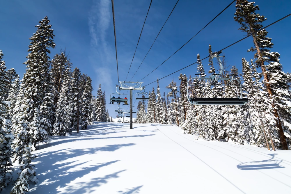 A snowy ski lift surrounded by evergreen trees under a clear blue sky.