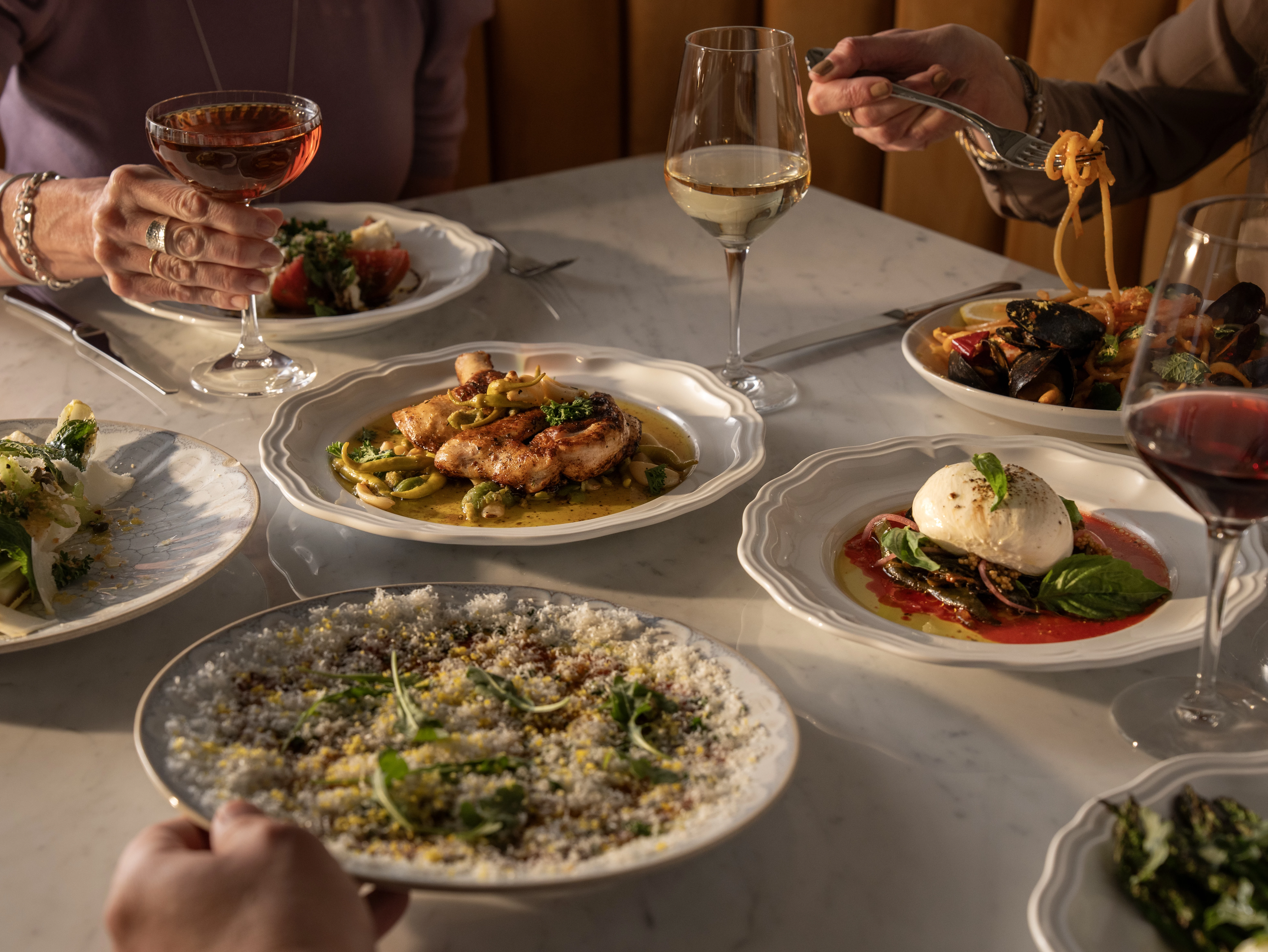 A table set with various dishes and glasses of wine, with people eating and drinking.