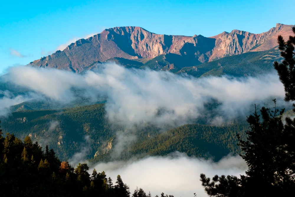 A mountain range with clouds and trees in the foreground.
