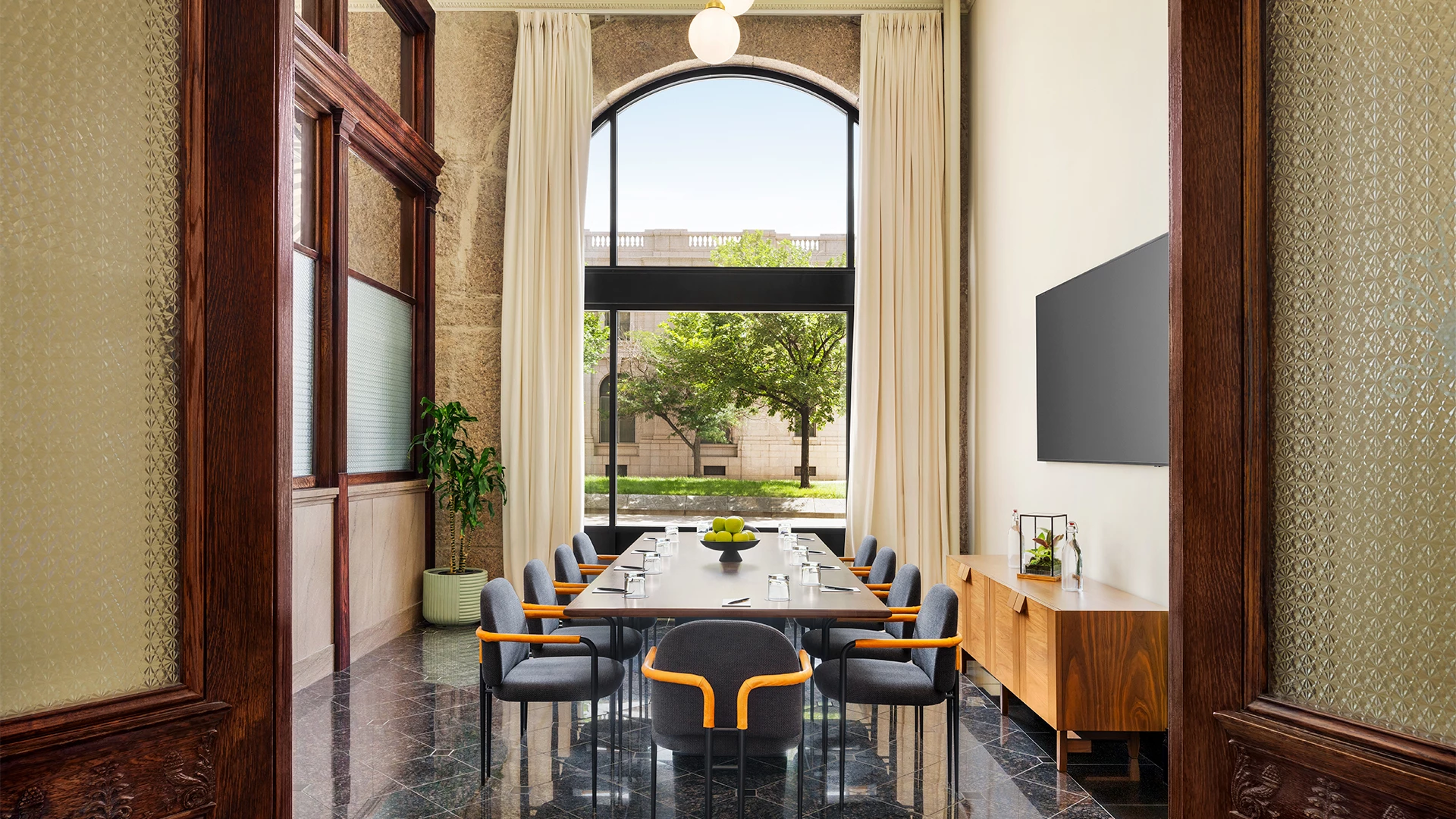 A large meeting room with a long table, chairs, and a TV on the wall.