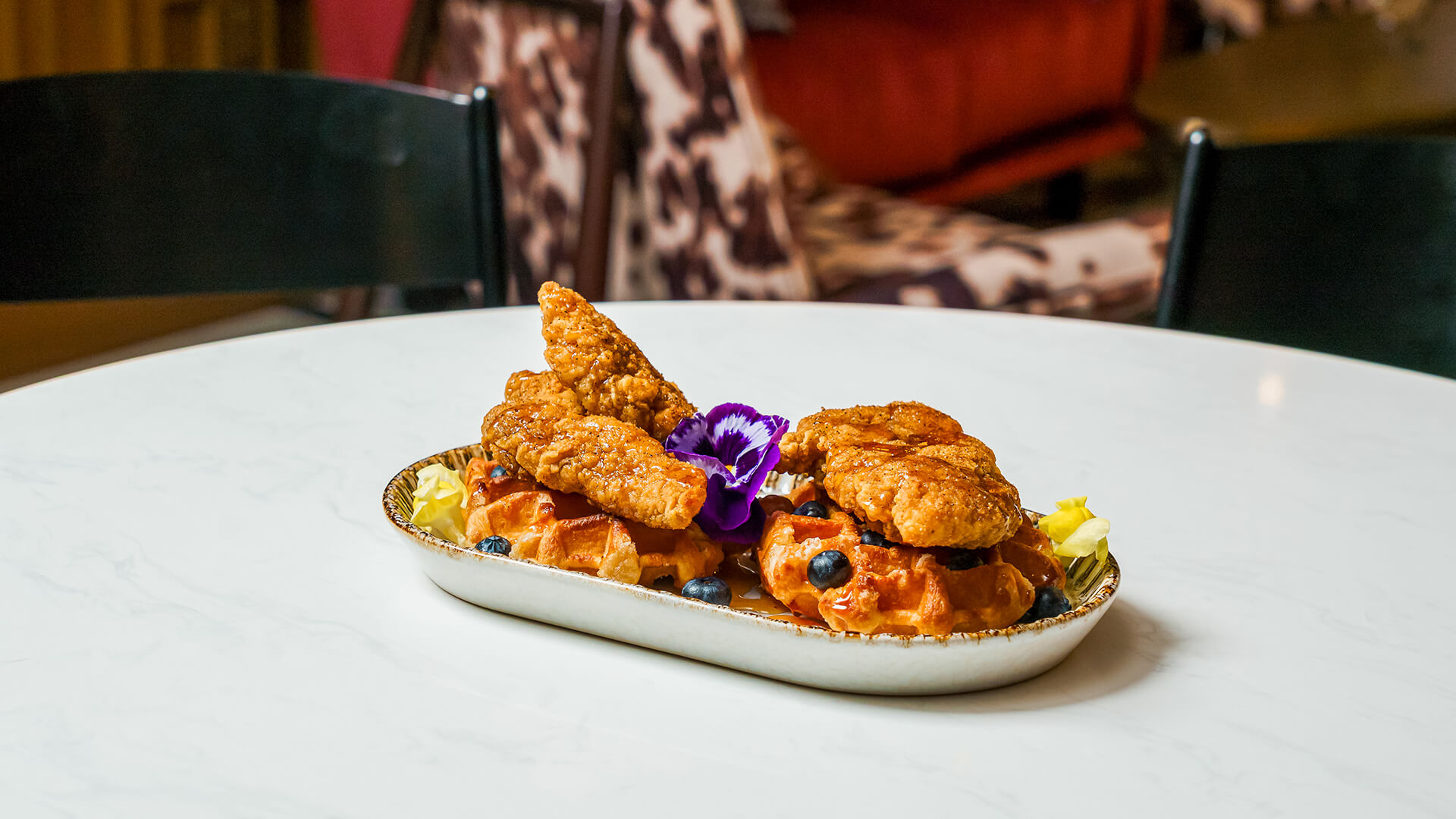 breaded cutlets served over waffles with blueberries and a purple flower