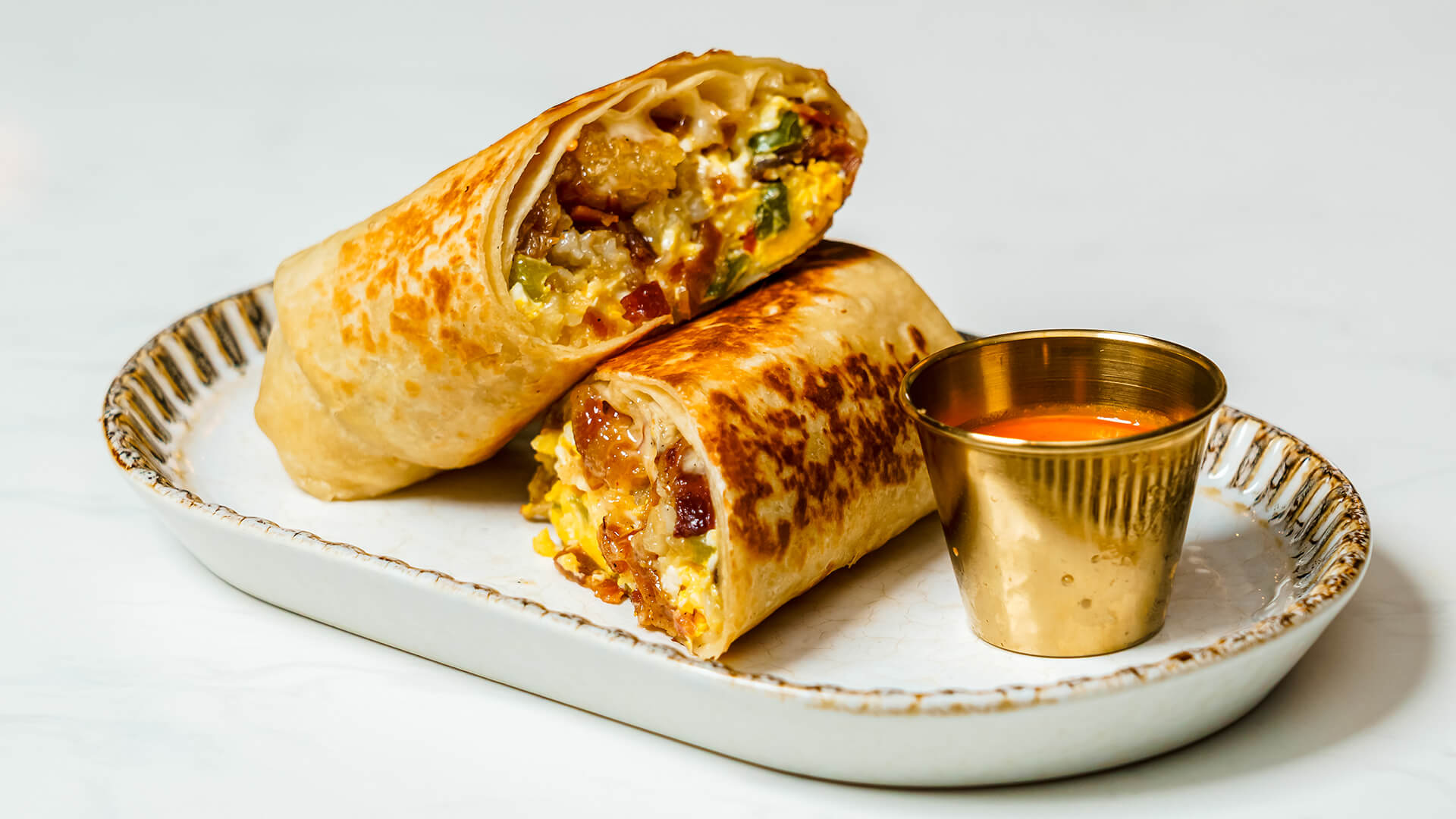 a burrito with a small cup of sauce