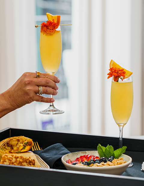 a hand holding a glass of yellow liquid with orange flowers