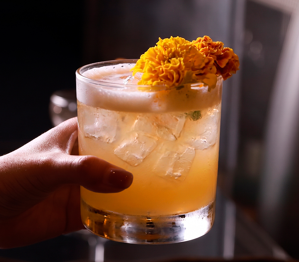 a hand holding a glass of liquid with ice and flowers